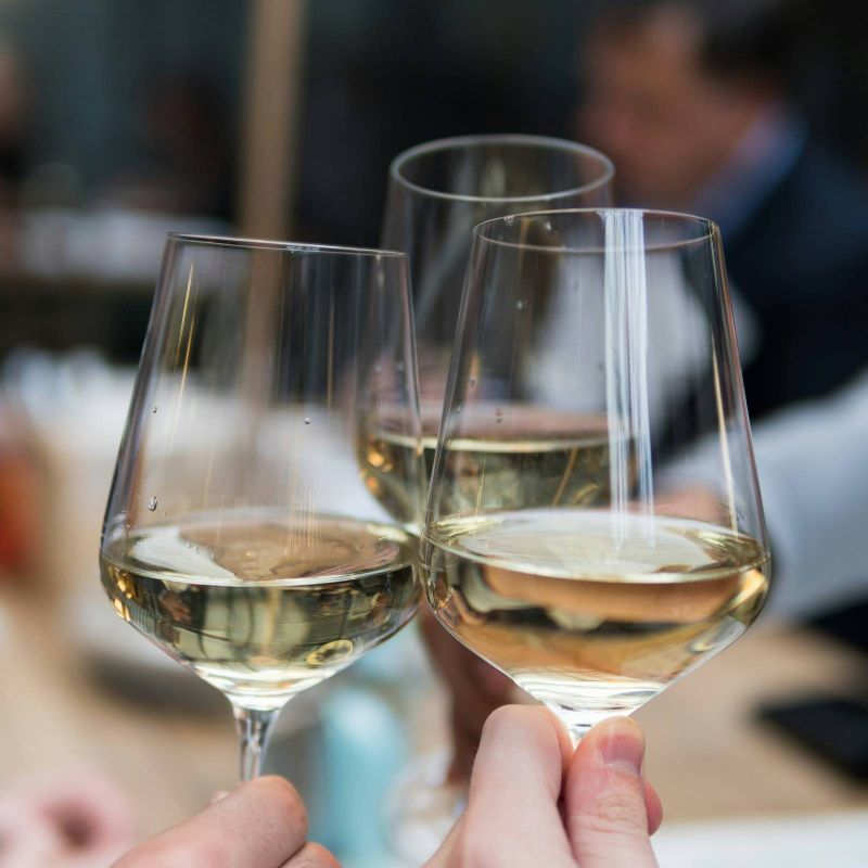 Three people clinking glasses of white wine together in a celebratory toast.