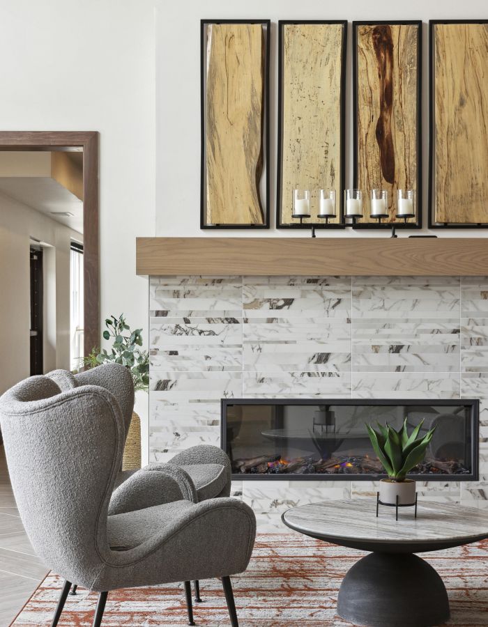 Modern living room with a gray armchair, round coffee table, and marble fireplace under wood artwork.
